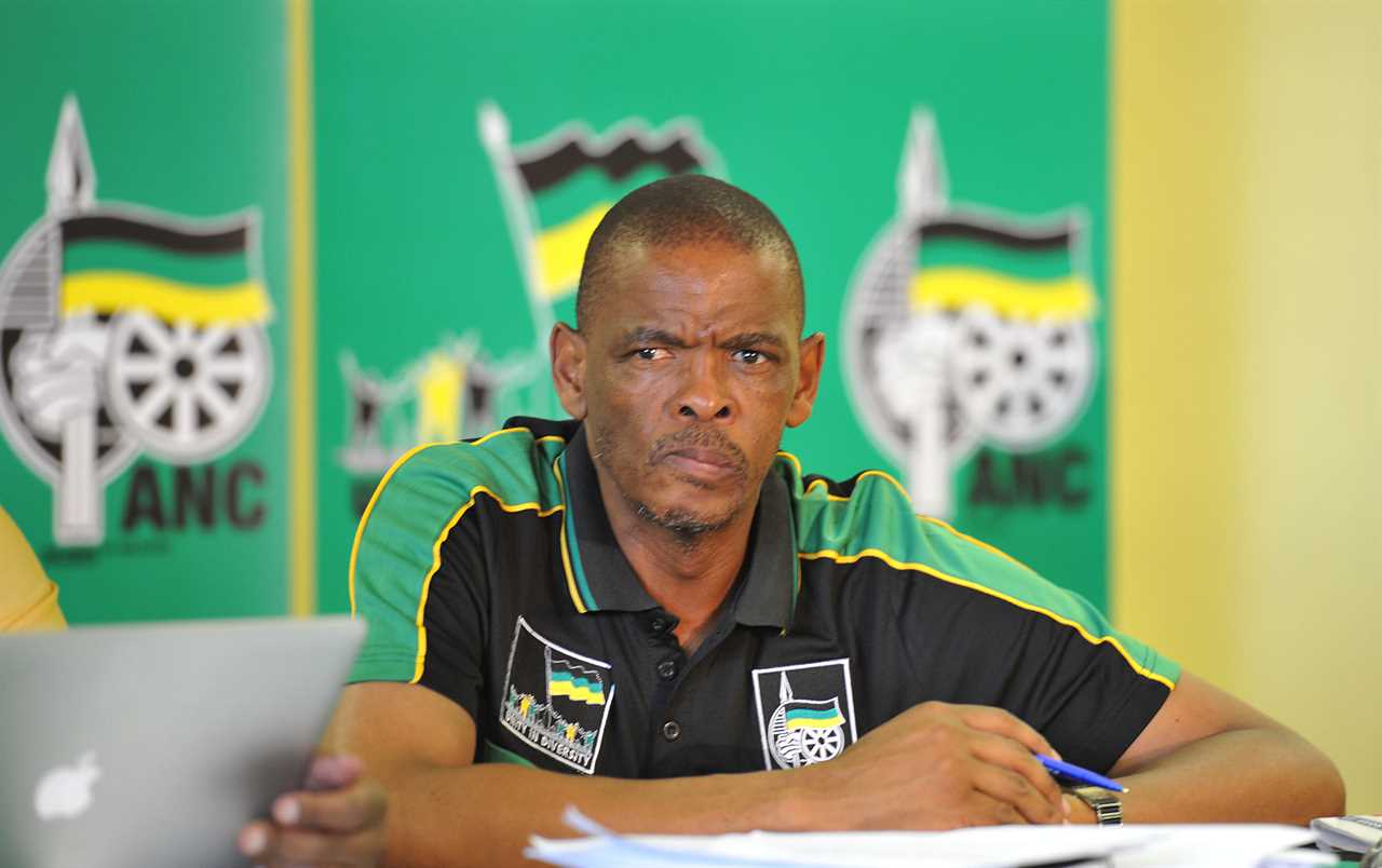 A man sitting in a chair and wearing a golf shirt in ANC colours looks in the distance.