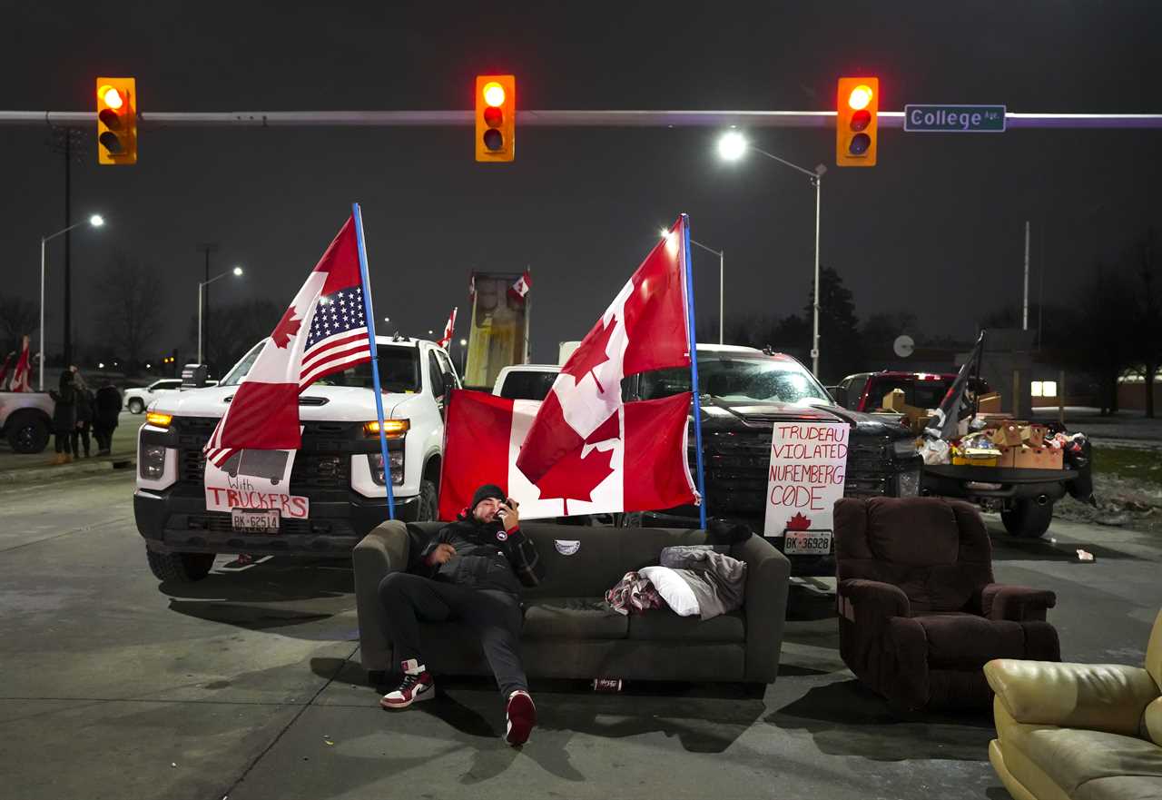 A trucker supporter sits on a couch as they block the access leading from the Ambassador Bridge, linking Detroit and Windsor, Windsor, Ont., February 9, 2022. (Nathan Denette/The Canadian Press)